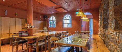 A restaurant with wooden tables and chairs, a stone wall, and arched windows.