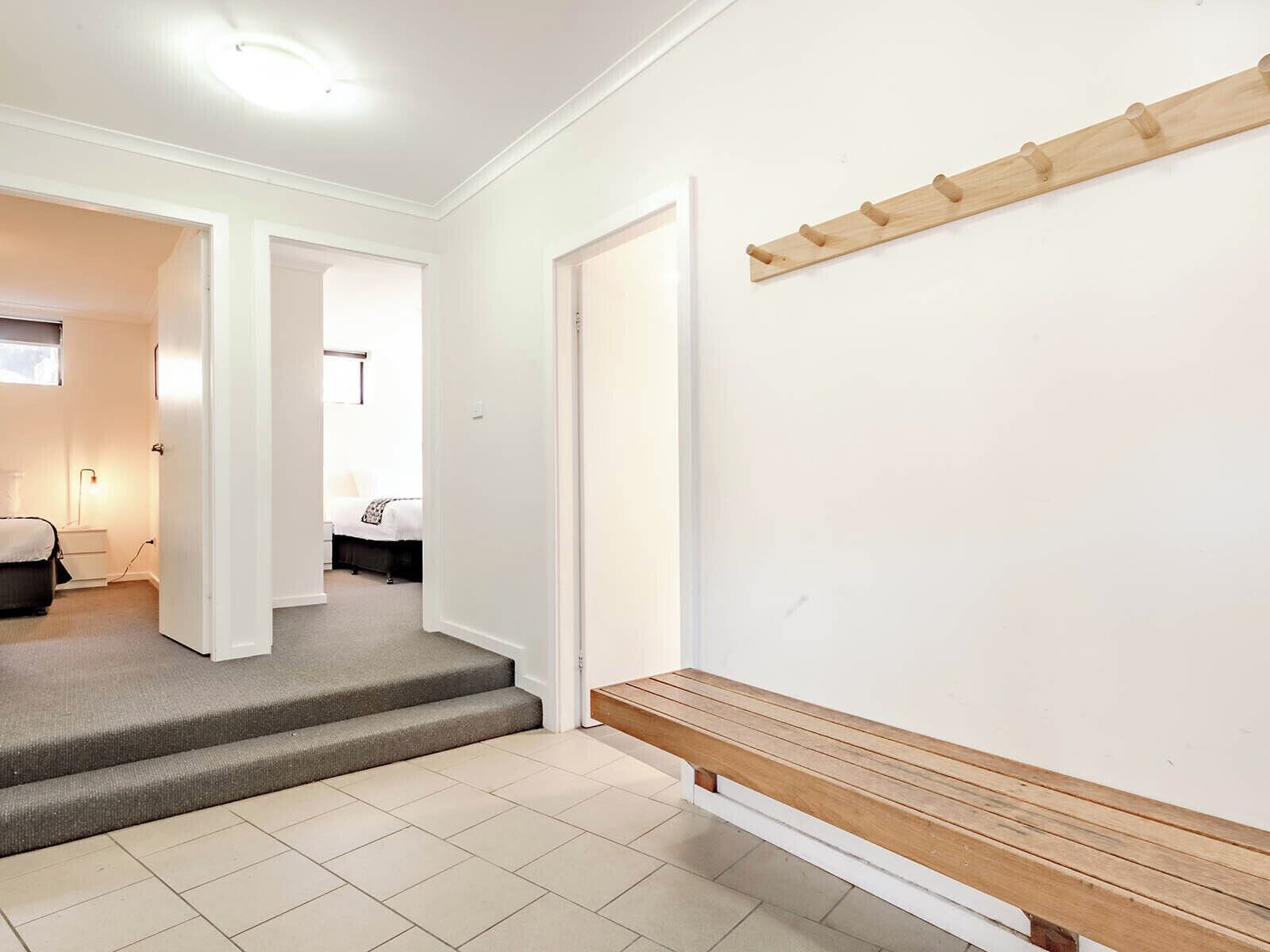 A hallway with a wooden bench, a coat rack, and a staircase leading to another room.
