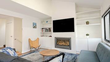 A modern living room with a fireplace, a flat-screen TV, and a bookshelf.