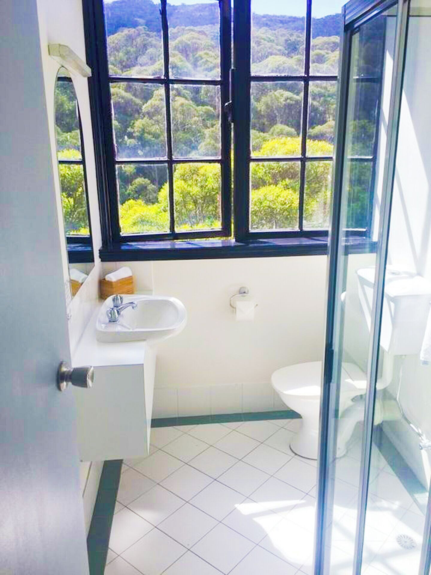 Ein Badezimmer mit großem Fenster, Waschbecken, Toilette und Duschkabine aus Glas.