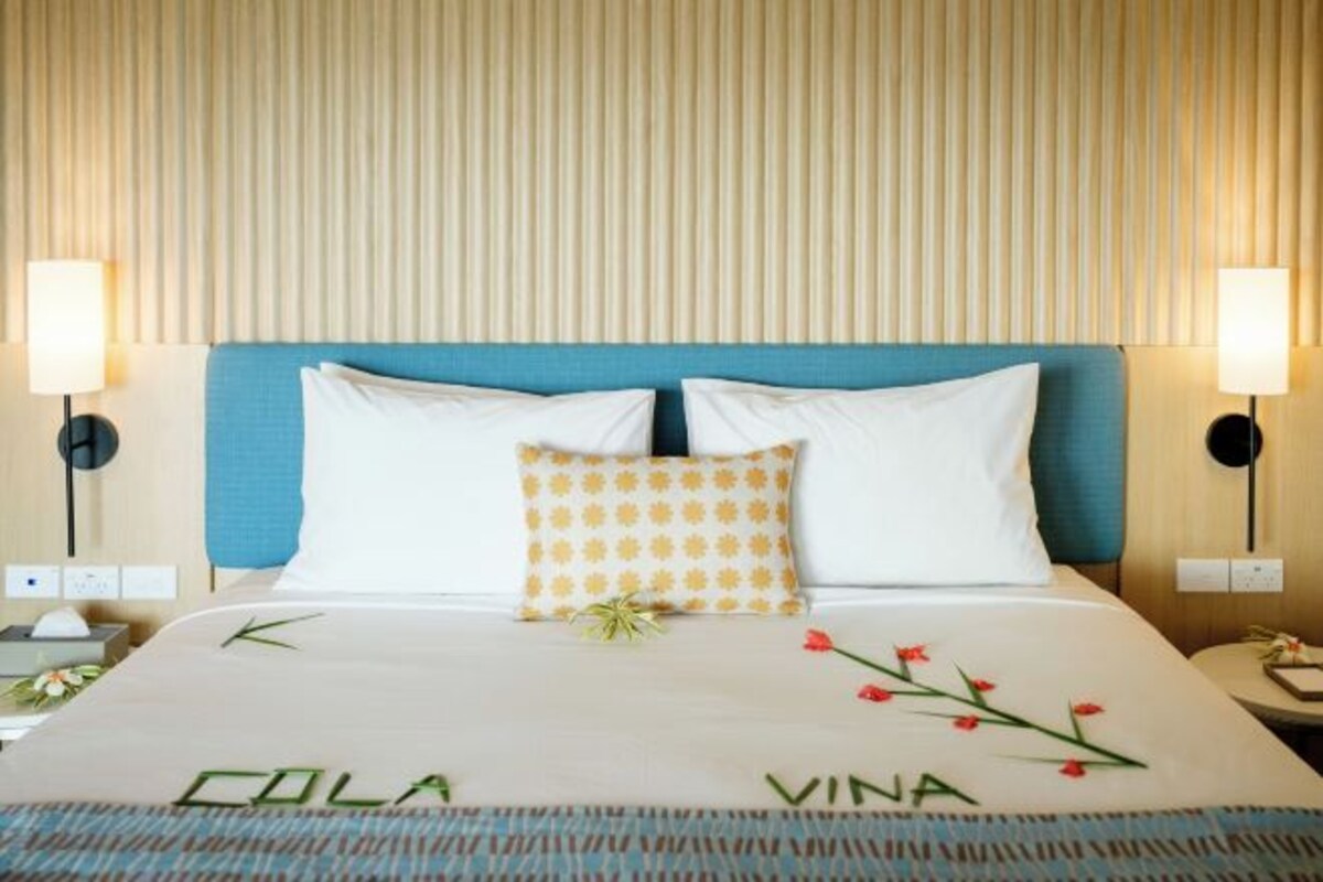 A hotel room with a bed, two bedside lamps, a nightstand, and a wall with vertical blinds.