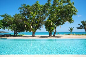 A clear blue pool surrounded by trees and a sandy beach. - Yatule Resort & Spa (Natadola)