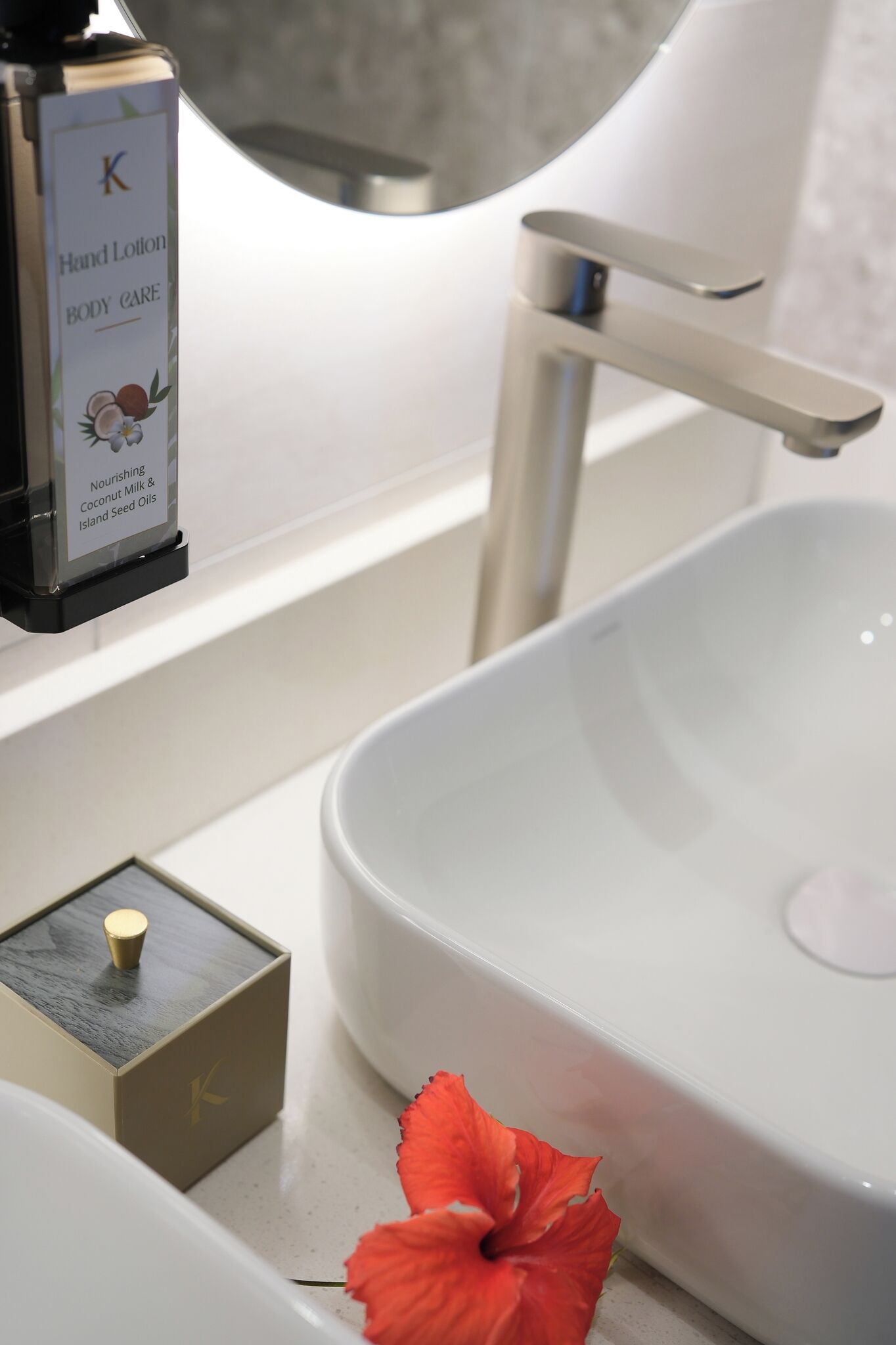 Un baño con un lavamanos blanco, un dispensador de crema de manos y una pequeña caja con una vela.