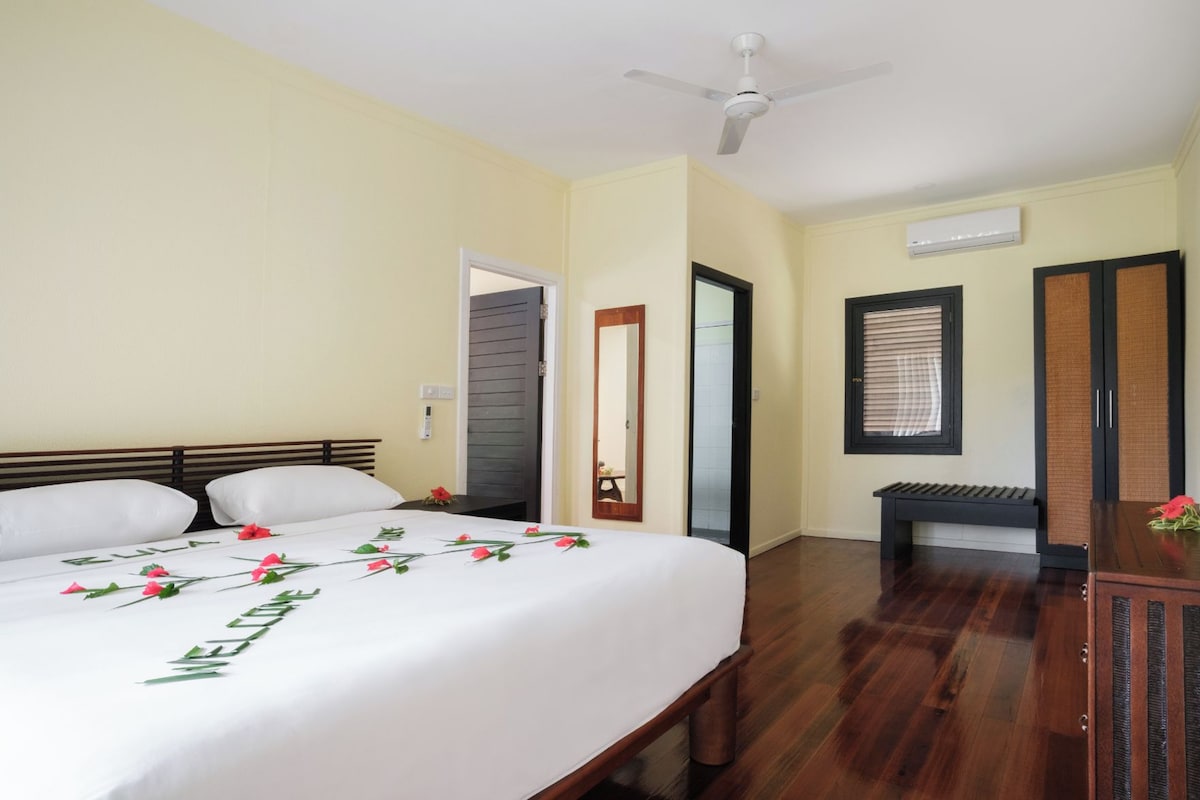 A hotel room with a bed, a desk, a chair, a ceiling fan, and an air conditioning unit.