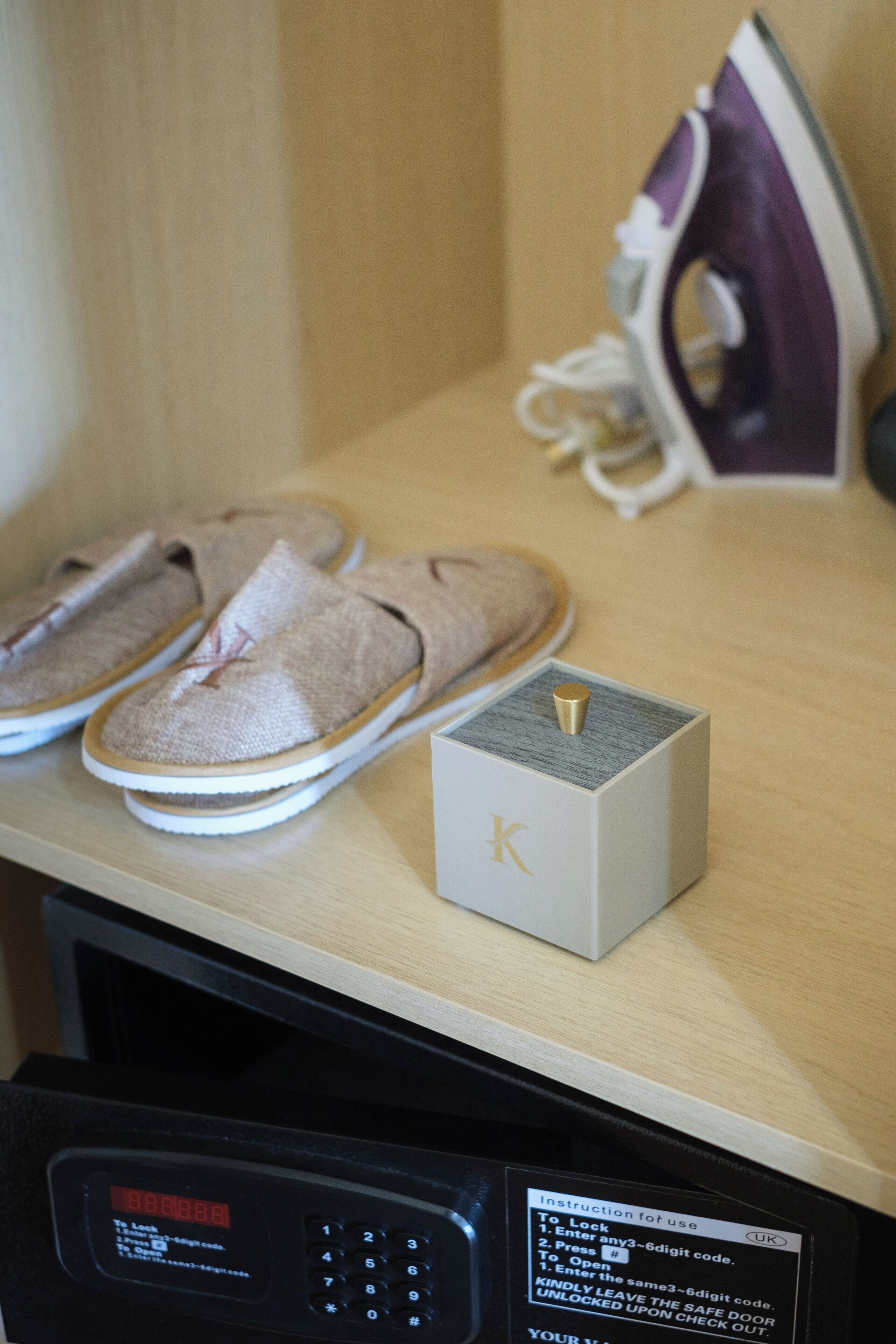 A microwave with a digital display, a pair of slippers, a small box with a 'K' on it, and an iron on a wooden surface.