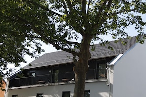 Ein zweistöckiges Gebäude mit Balkon und Baum davor.
