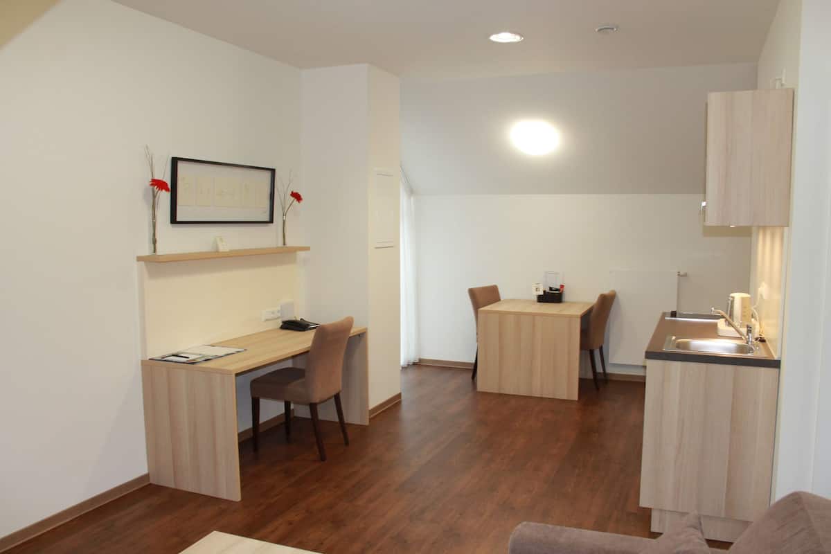 Un espace de vie compact comprenant un bureau en bois, une table à manger et un coin cuisine.