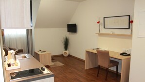 A compact hotel room with a kitchenette, a desk, a chair, a TV mounted on the wall, and a small potted plant. - Prime 20 Serviced Apartments (Frankfurt)