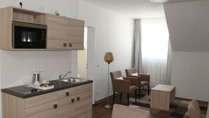 A modern kitchen with a microwave, sink, and wooden cabinets. There are two chairs and a small table in a dining area with a view of a window. - Prime 20 Serviced Apartments (Frankfurt)