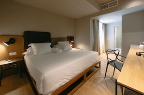 A hotel room with a bed, bedside tables, a desk, and a chair.