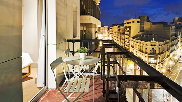 A balcony with a table and chairs, overlooking a cityscape at night. - One Shot Colón (Valencia)