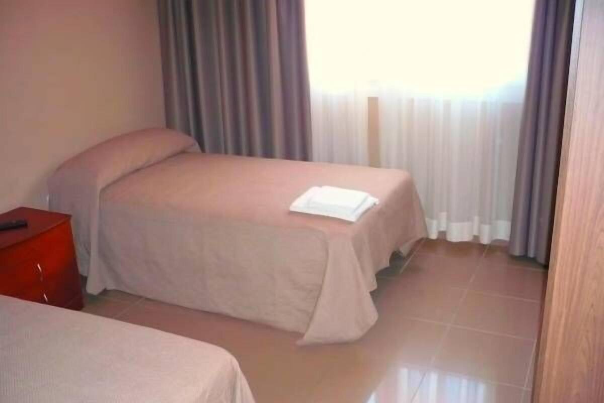 Habitación de hotel con dos camas, una mesita de noche roja y una ventana con cortinas.