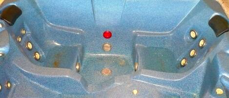 Una bañera de hidromasaje azul con un panel de control, múltiples chorros y un botón rojo.