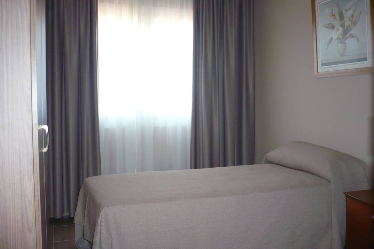 Una habitación de hotel con una cama, una puerta de madera y una ventana con cortinas.