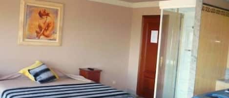 A bedroom with a bed, a bedside table, a nightstand, a painting on the wall, and a door leading to another room.
