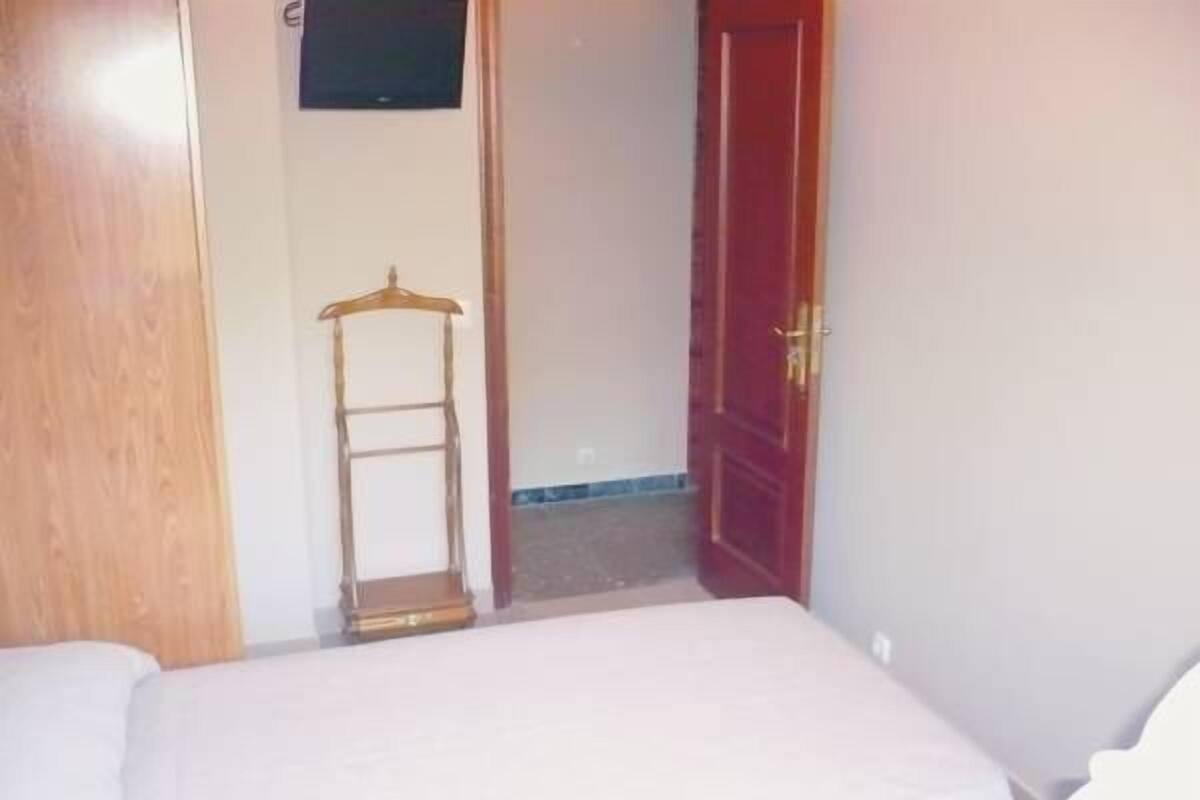 Una habitación con una cama, un perchero de madera, un televisor en la pared y una puerta roja.