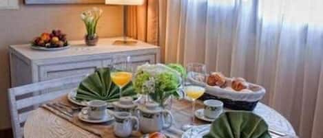 A breakfast table set with plates, cups, a fruit bowl, and a decorative leaf arrangement.