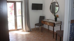 Une chambre dotée d’une porte-fenêtre coulissante, d’un téléviseur à écran plat, d’un miroir, d’un bureau avec une chaise et d’une plante en pot.