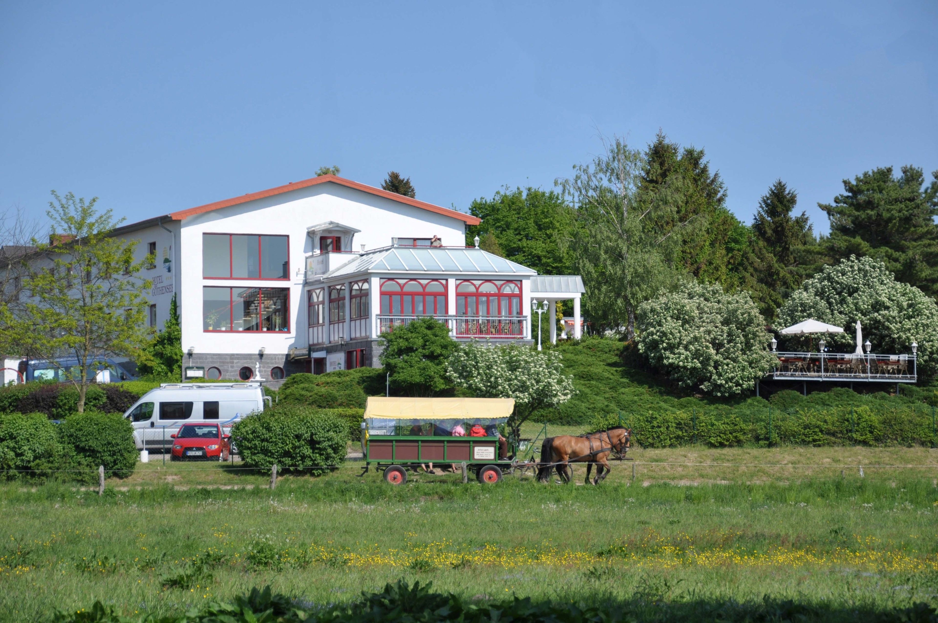 Une grande maison blanche avec un toit rouge, un attelage et un cheval.