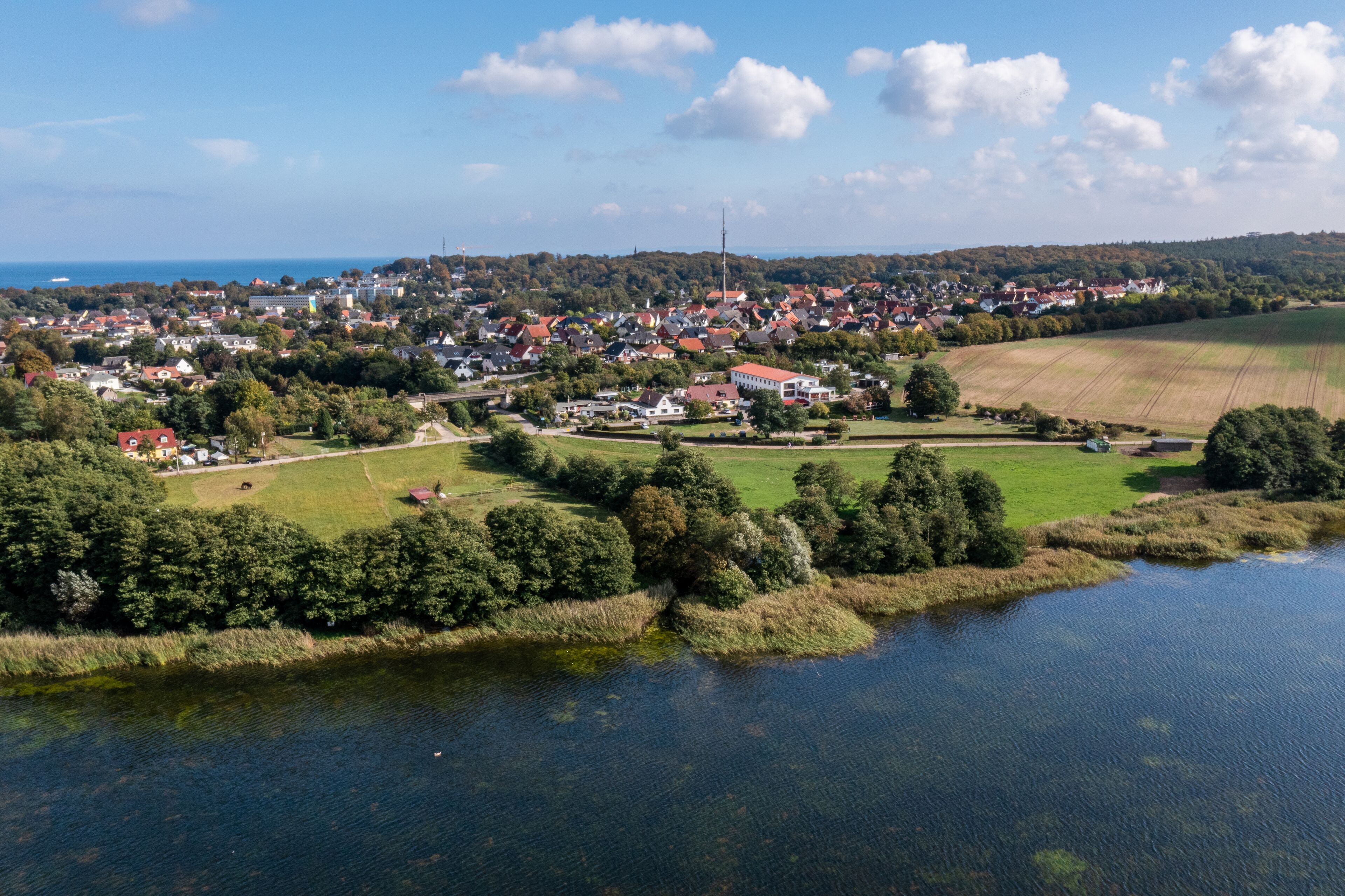 Une petite ville située au bord d’une rivière, avec des maisons, une église et un champ.