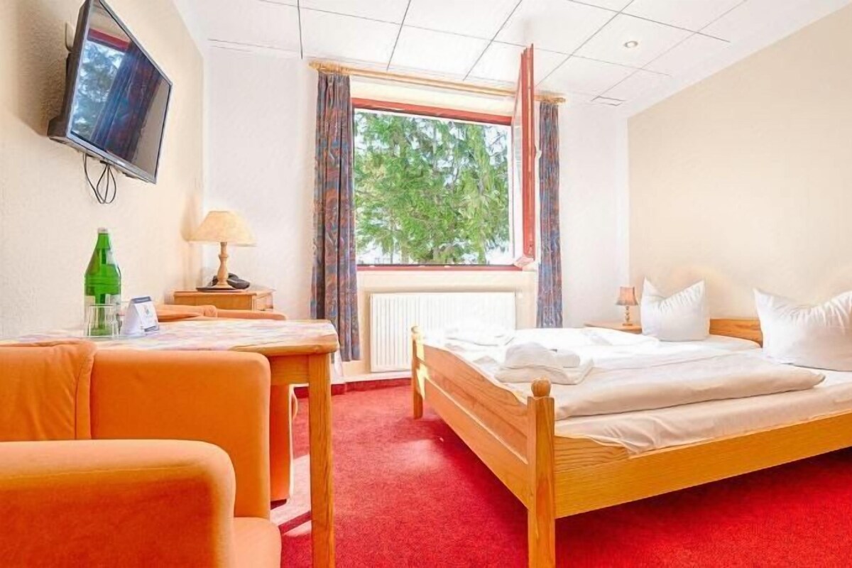 Habitació d'hotel amb llit, escriptori, cadira, televisió i finestra amb cortines.