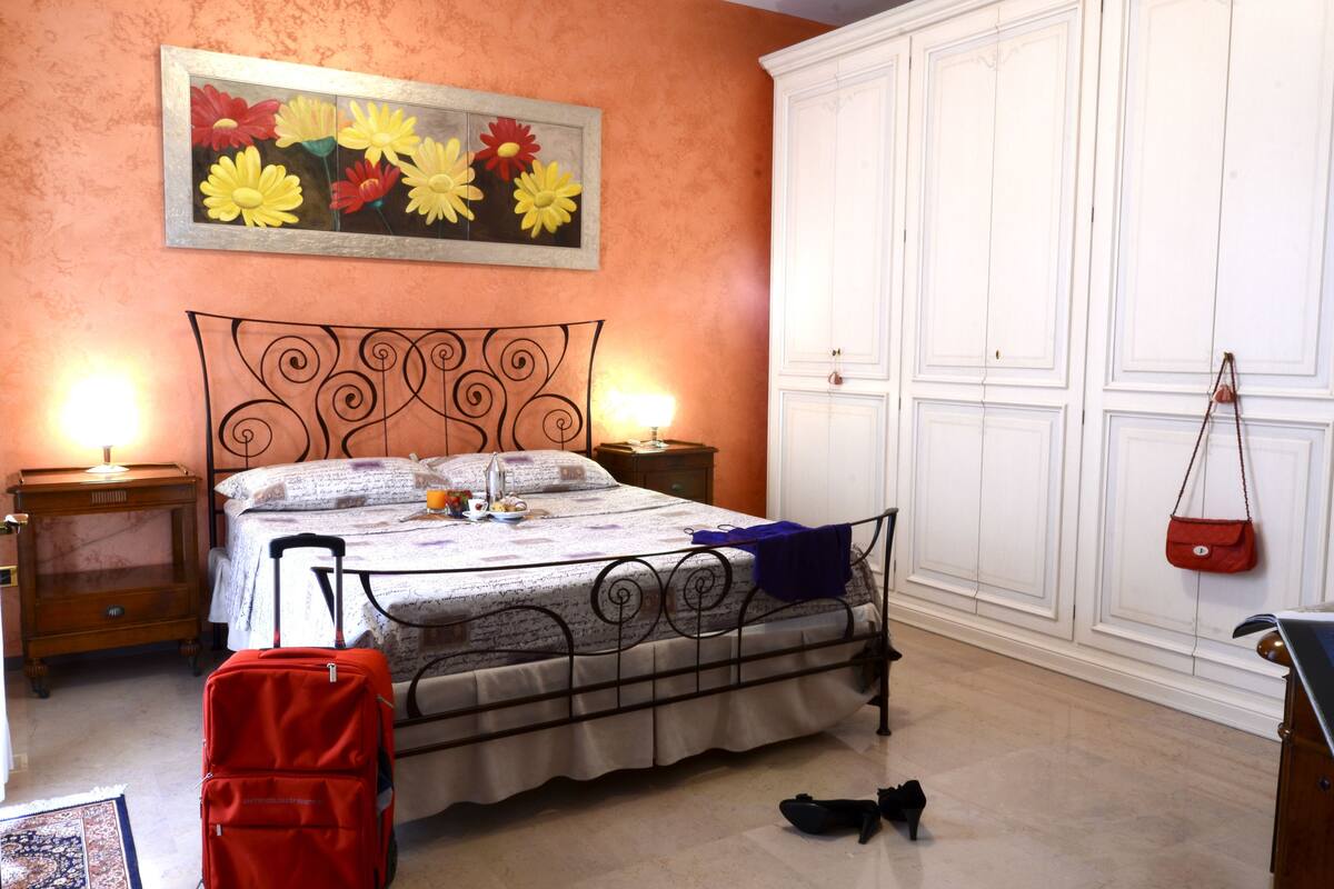 A bedroom with a bed, nightstands, a dresser, a painting, and a suitcase.