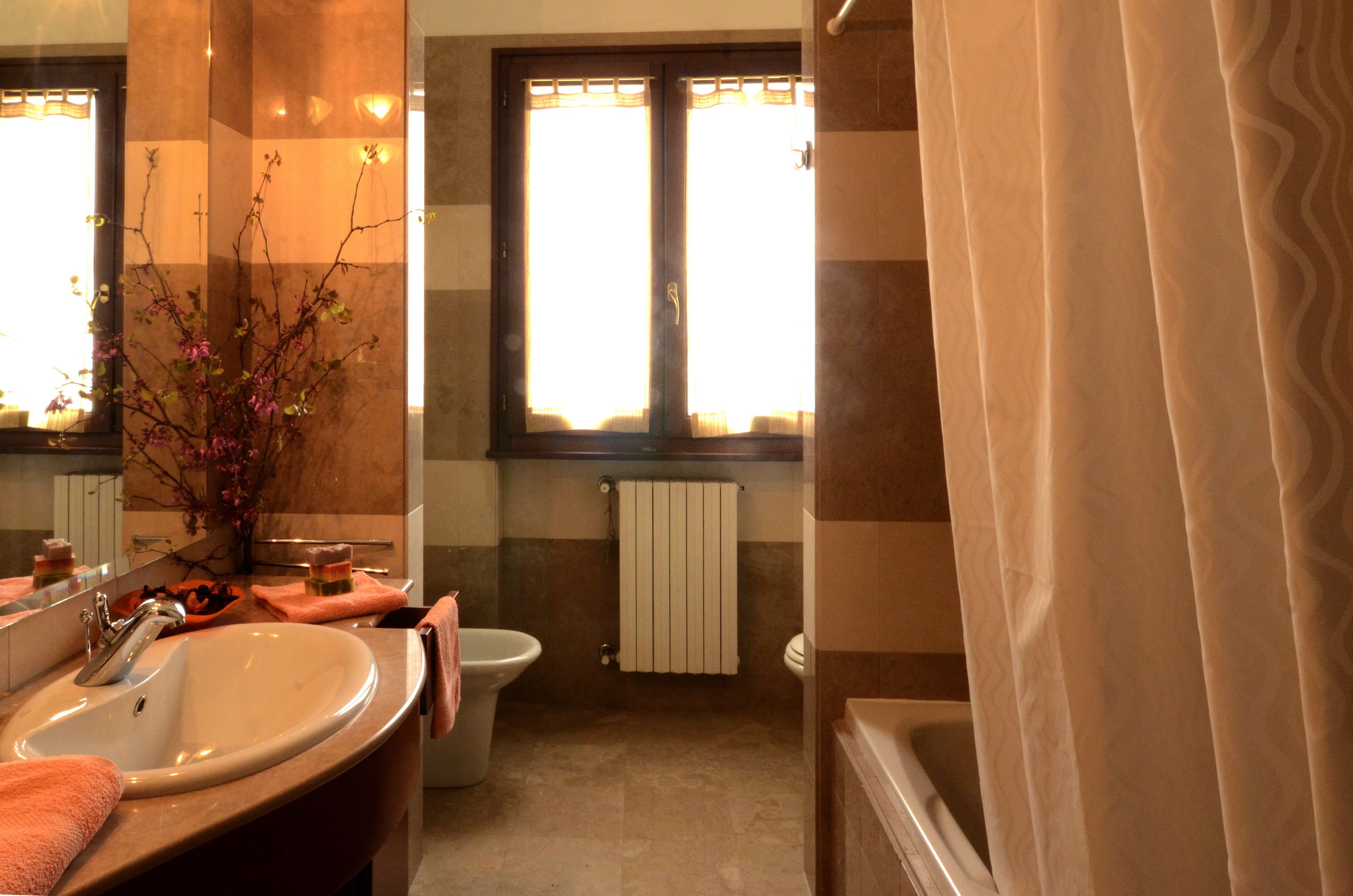 A bathroom with a sink, toilet, and bathtub. There is a window with curtains and a radiator above the toilet.