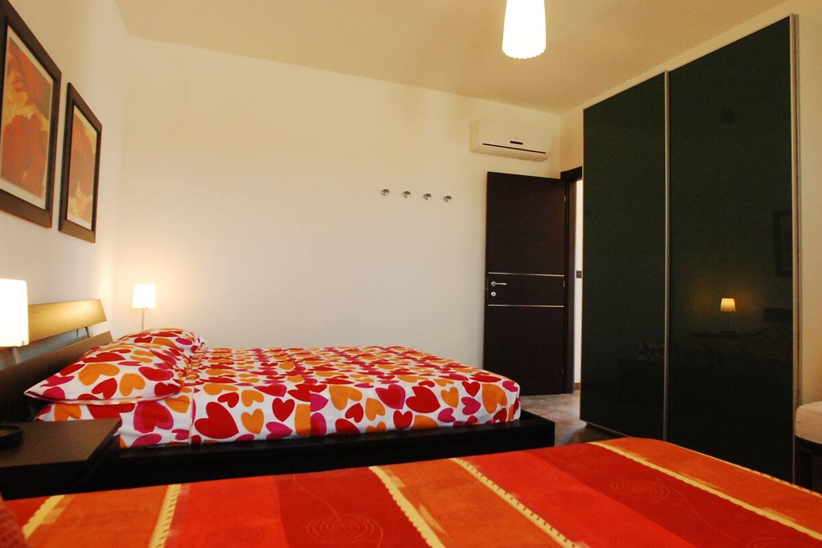 A hotel room with a bed, a nightstand, a lamp, a wardrobe, and an air conditioning unit.
