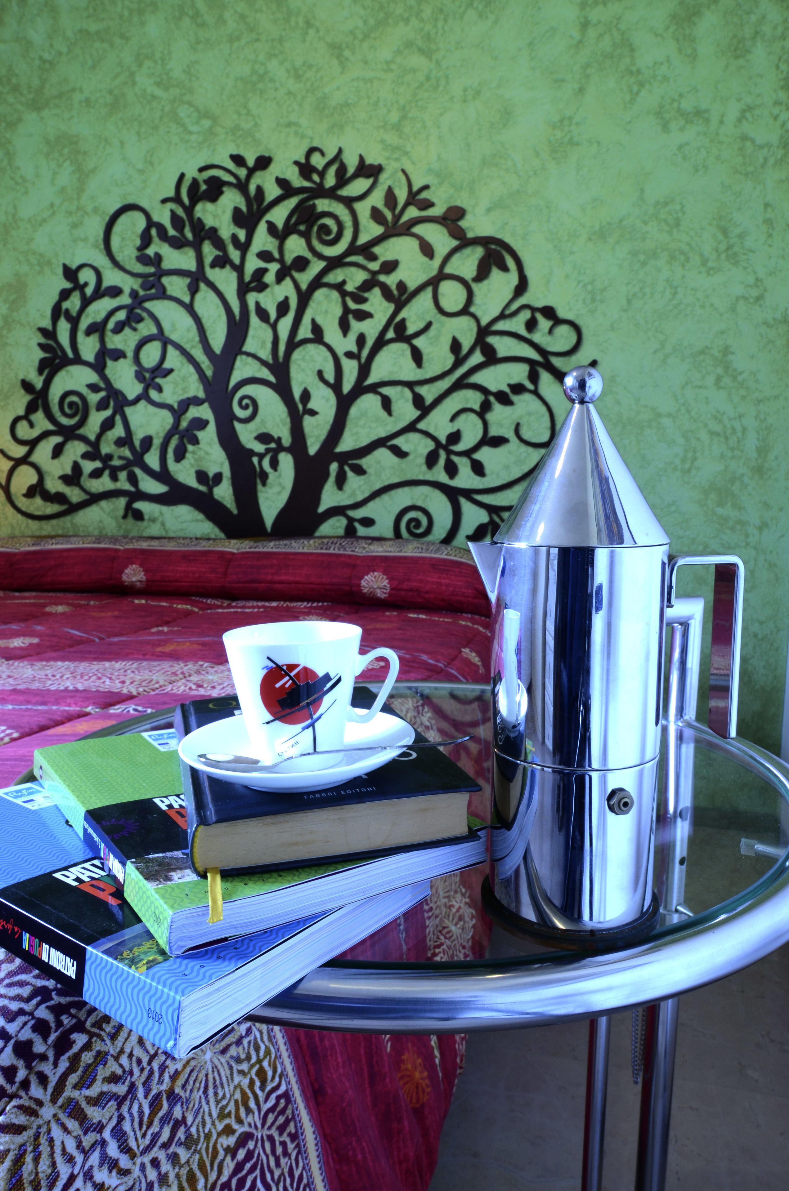 A coffee maker on a glass table with a cup and books.