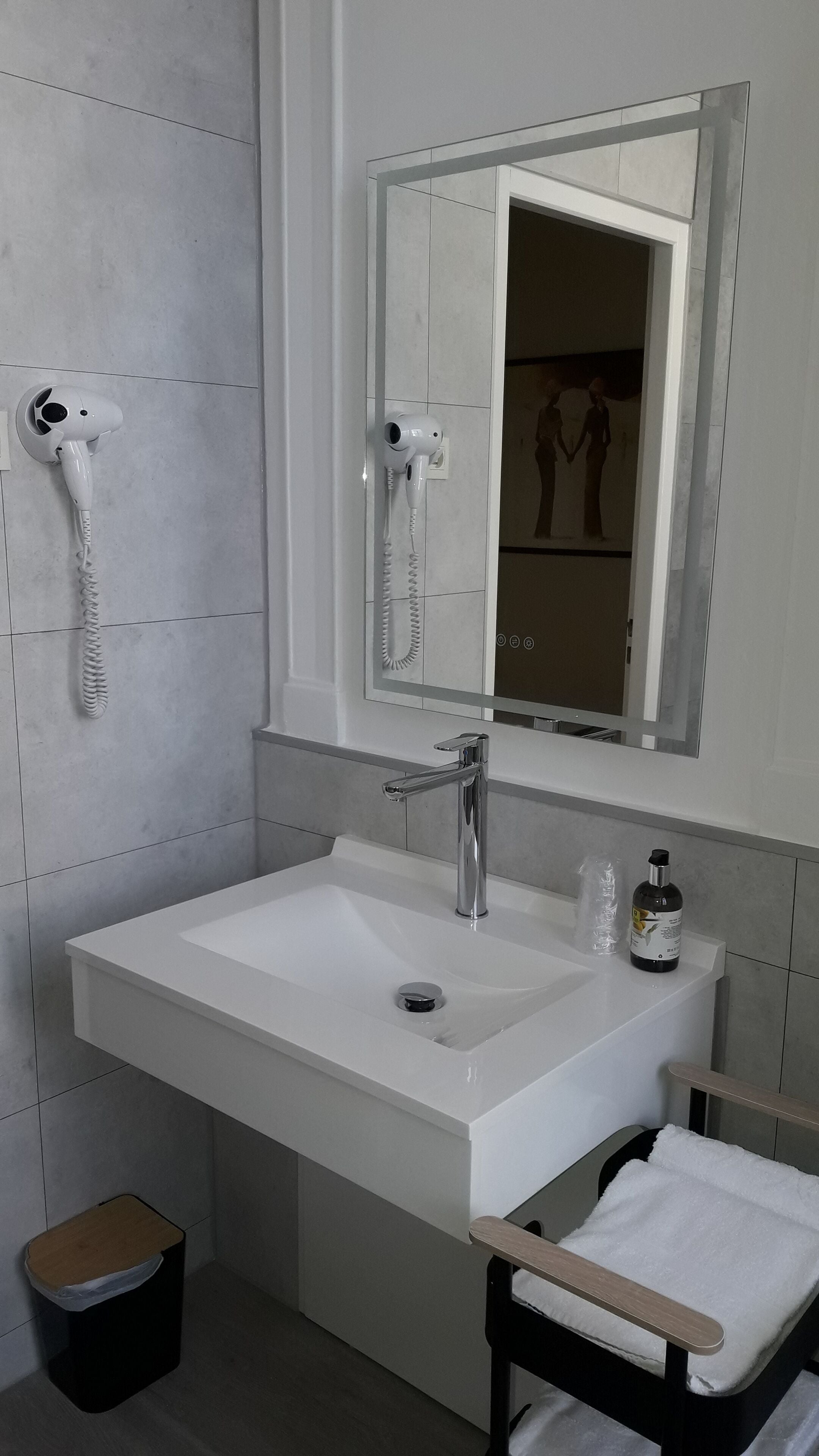 A modern bathroom with a white sink, a mirror, and a hairdryer mounted on the wall.