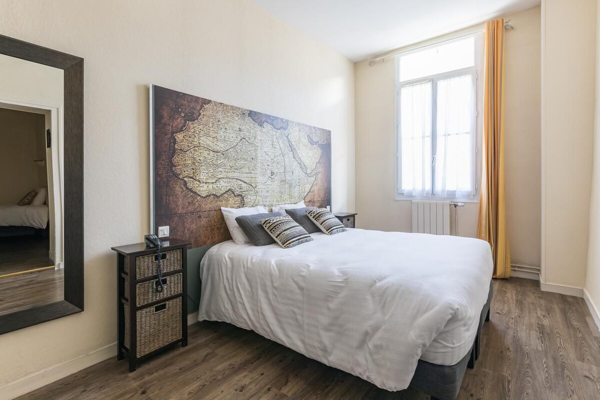 Un dormitorio con una cama grande, un cuadro de un mapa en la pared, una mesita de noche y una ventana con cortinas.