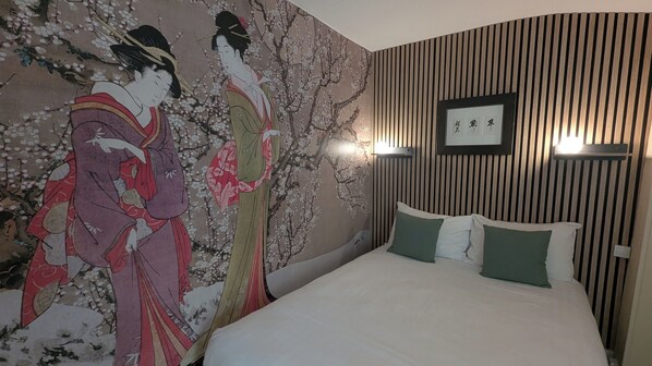 A hotel room with a large mural of cherry blossoms, a bed with white bedding and green pillows, and a wall-mounted light fixture. - Hôtel La Fayette (Rochefort)