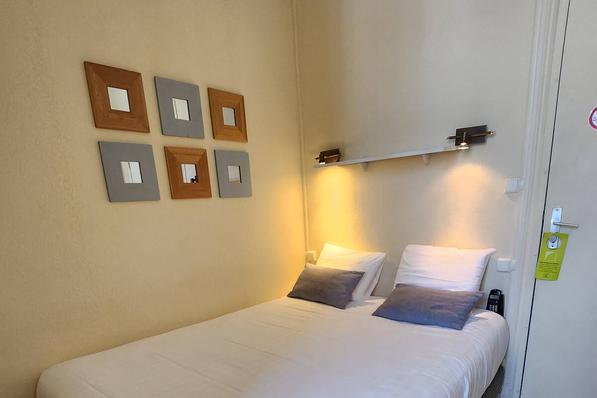 A single bed with white bedding, a wooden floor, and a wall with framed mirrors.
