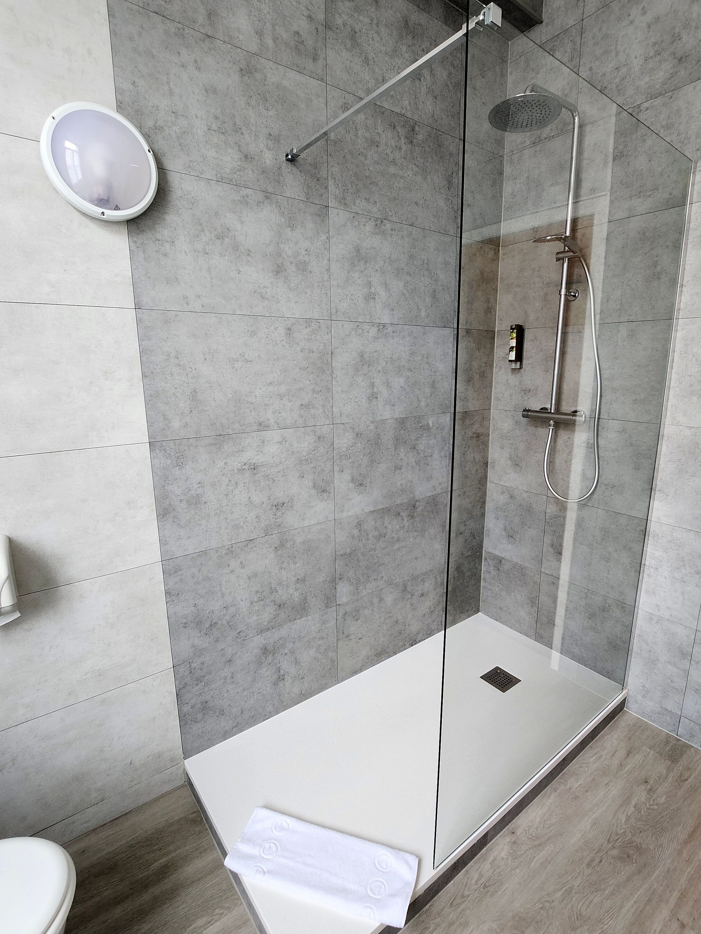 Une salle de bain moderne avec une douche à parois de verre, des toilettes blanches et une serviette sur le sol.