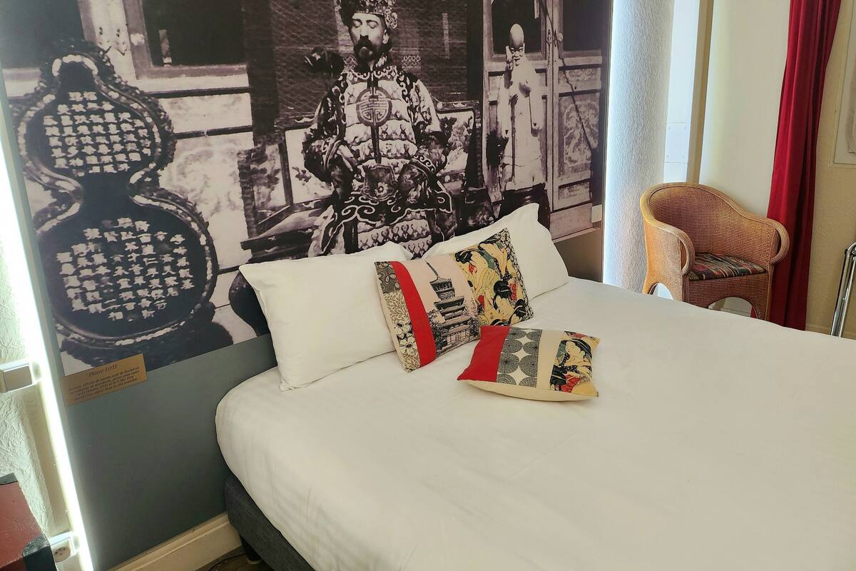 A hotel room with a large bed, a wicker chair, and a wall mural.