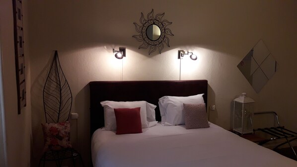 Una cama bien hecha con almohadas blancas y rojas, un cabecero oscuro y luces fijadas a la pared.