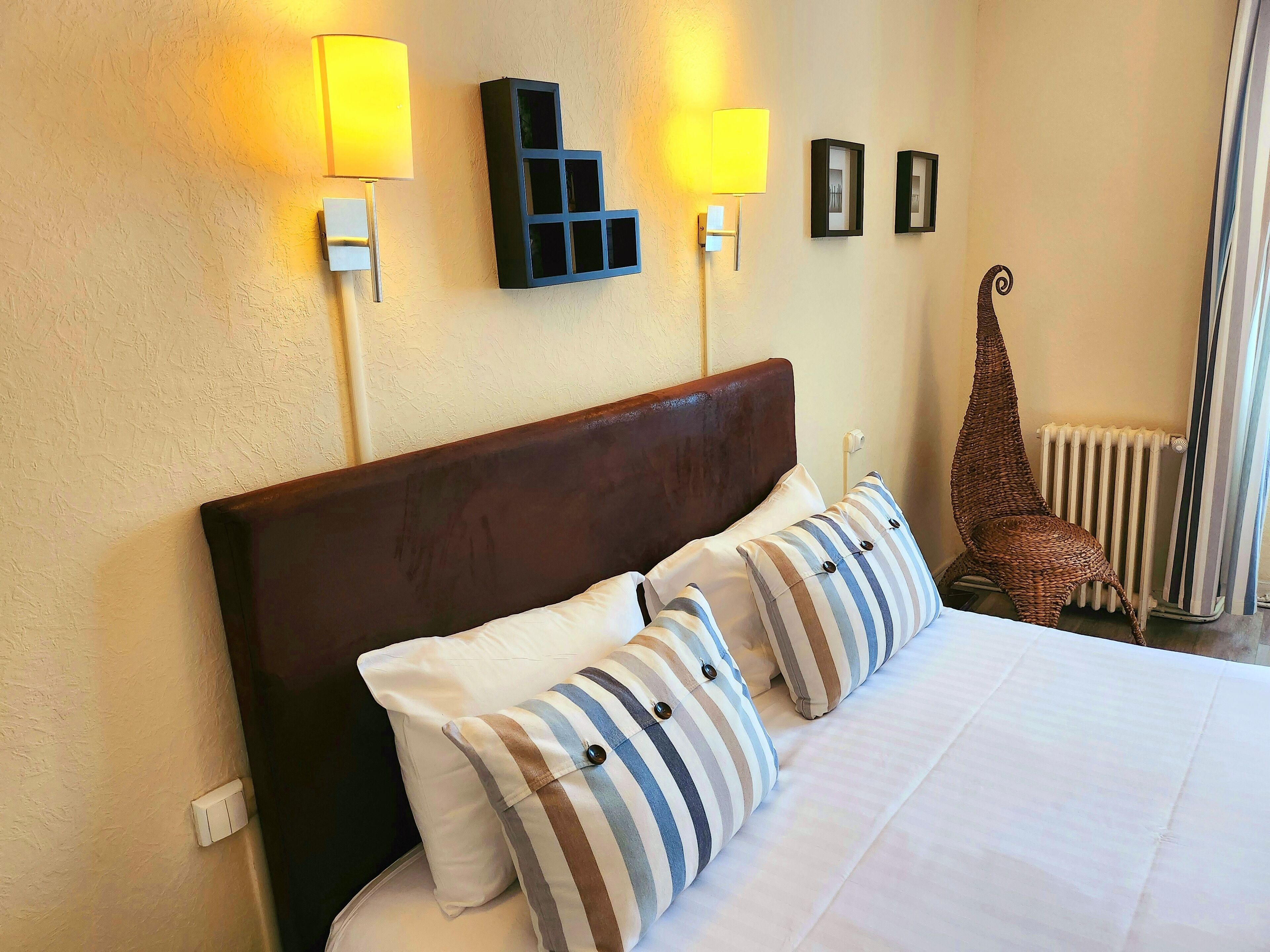 Een net opgemaakt bed met gestreepte kussens, een donker houten hoofdbord en twee wandlampen.