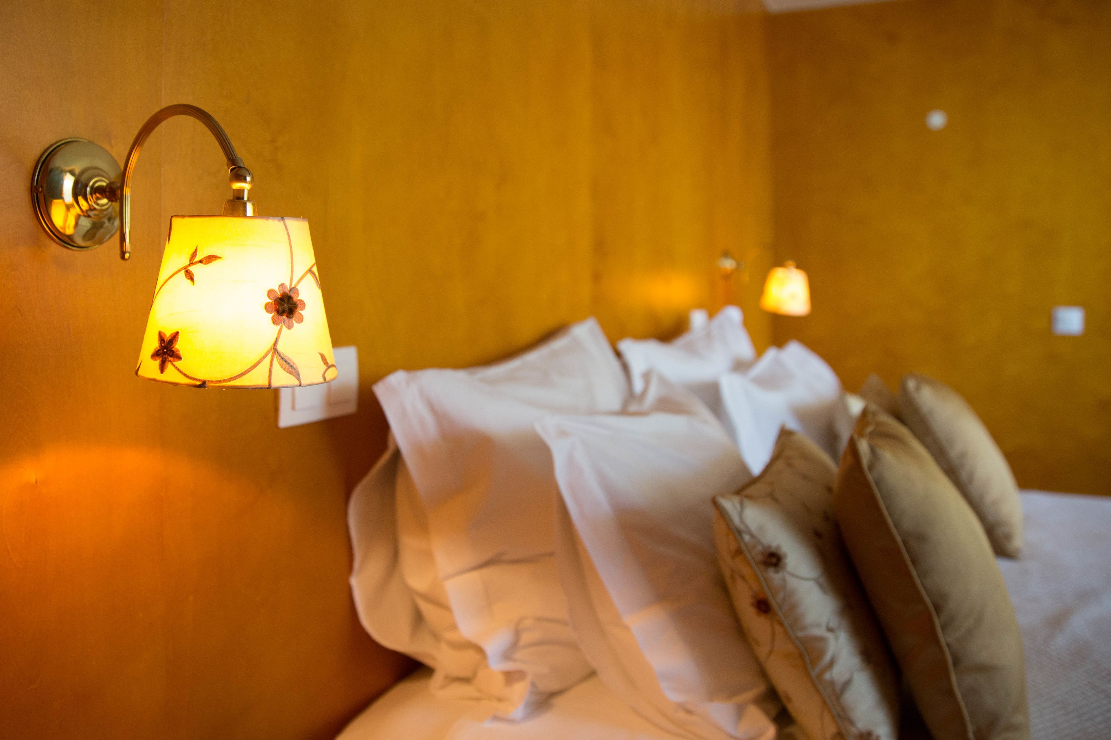 Een hotelkamer met een bed, kussens en een wandlamp.