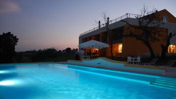Ein Swimmingpool mit weißem Sonnenschirm und Liegestühlen, umgeben von einem Gebäude mit Balkon und Außenbereich.