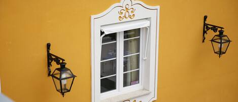 Un mur jaune avec une fenêtre à cadre blanc et deux lanternes noires fixées au mur.