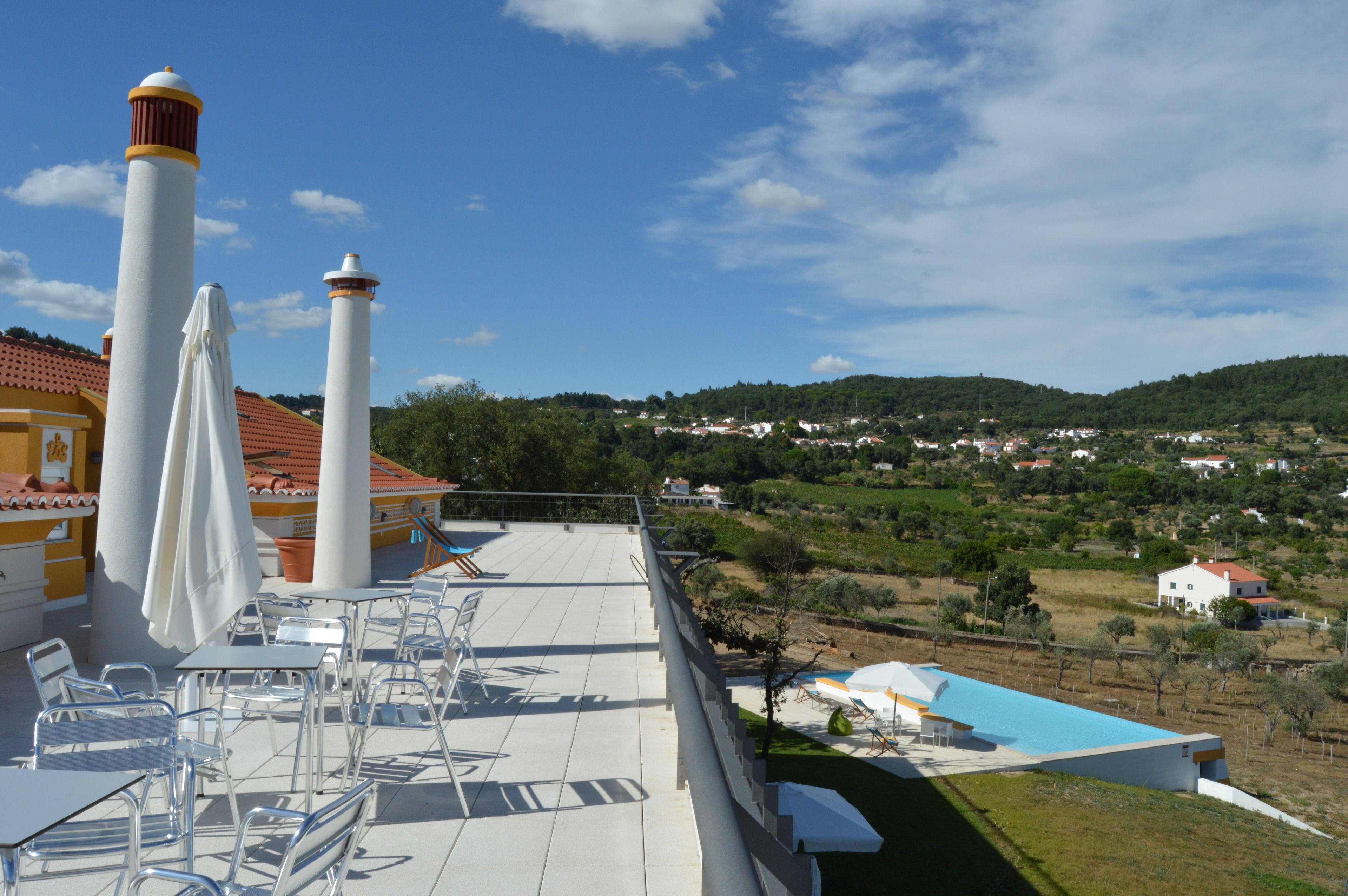 Une terrasse avec des sièges extérieurs et une piscine, offrant une vue sur un village perché sur une colline.