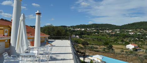 Une terrasse avec des sièges extérieurs et une piscine, offrant une vue sur un village perché sur une colline.