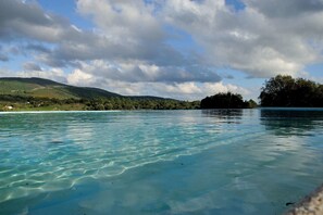 Una vista despejada de una playa con aguas turquesas, una colina boscosa a lo lejos y un cielo nublado.