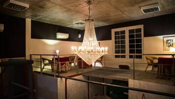 Una habitación con candelabro, ventana con persianas y una silla con mantel rojo.
