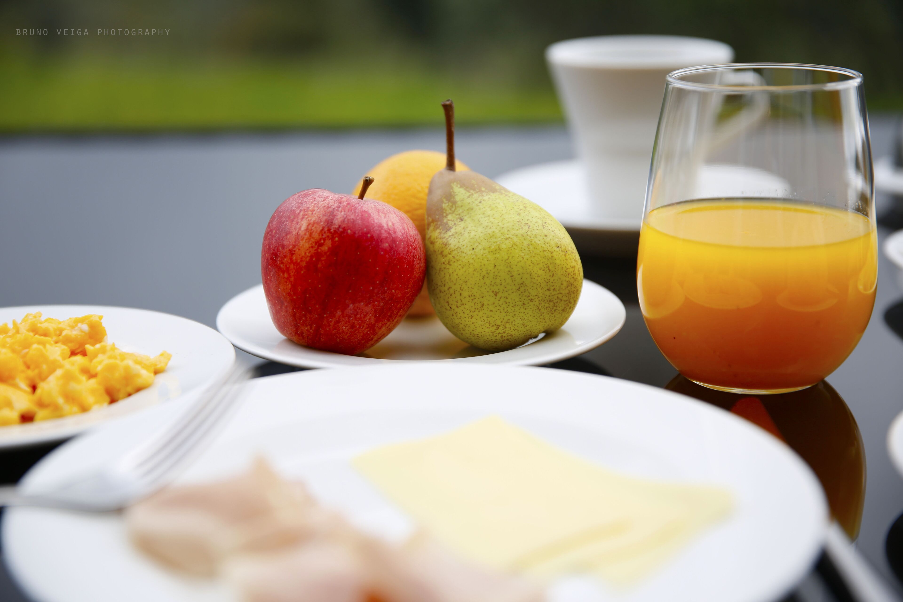 Desayuno con platos de comida, incluyendo una manzana, pera, jugo de naranja, huevos revueltos y tostadas.