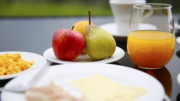 Desayuno con platos de comida, incluyendo una manzana, pera, jugo de naranja, huevos revueltos y tostadas.
