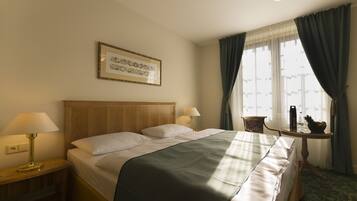 A hotel room with a large bed, two bedside lamps, a framed picture on the wall, a small table with a lamp, and a window with curtains.