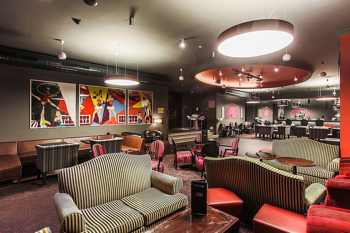 A modern lounge area with striped sofas, red chairs, and a bar area with stools.