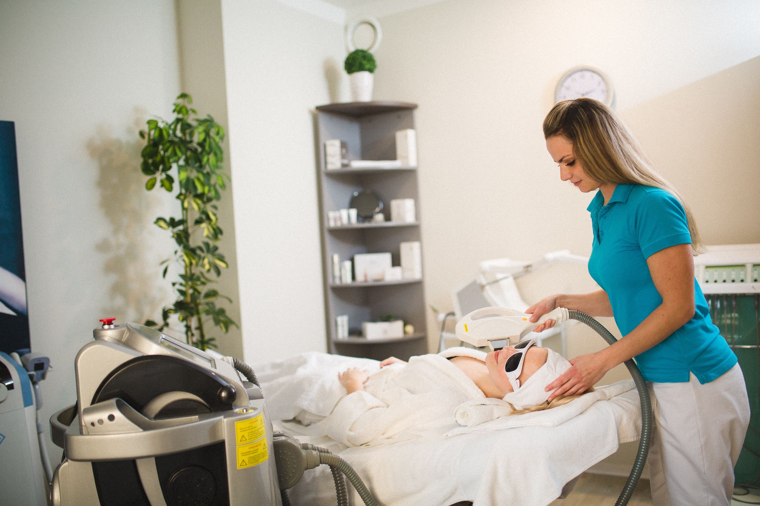 A medical treatment room with a patient lying on a bed, a healthcare professional attending to the patient, and medical equipment.