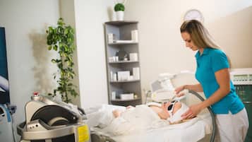 A medical treatment room with a patient lying on a bed, a healthcare professional attending to the patient, and medical equipment.